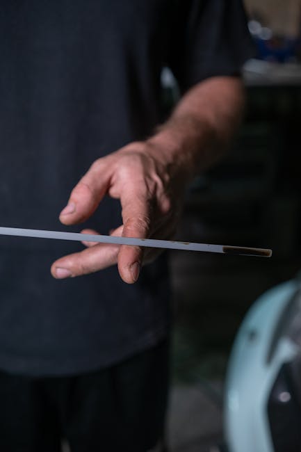 Detailed close-up of a hand holding a dipstick to check engine oil level in a garage setting.