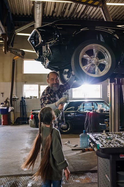 Father and daughter working together on a car repair in a bustling auto repair shop.